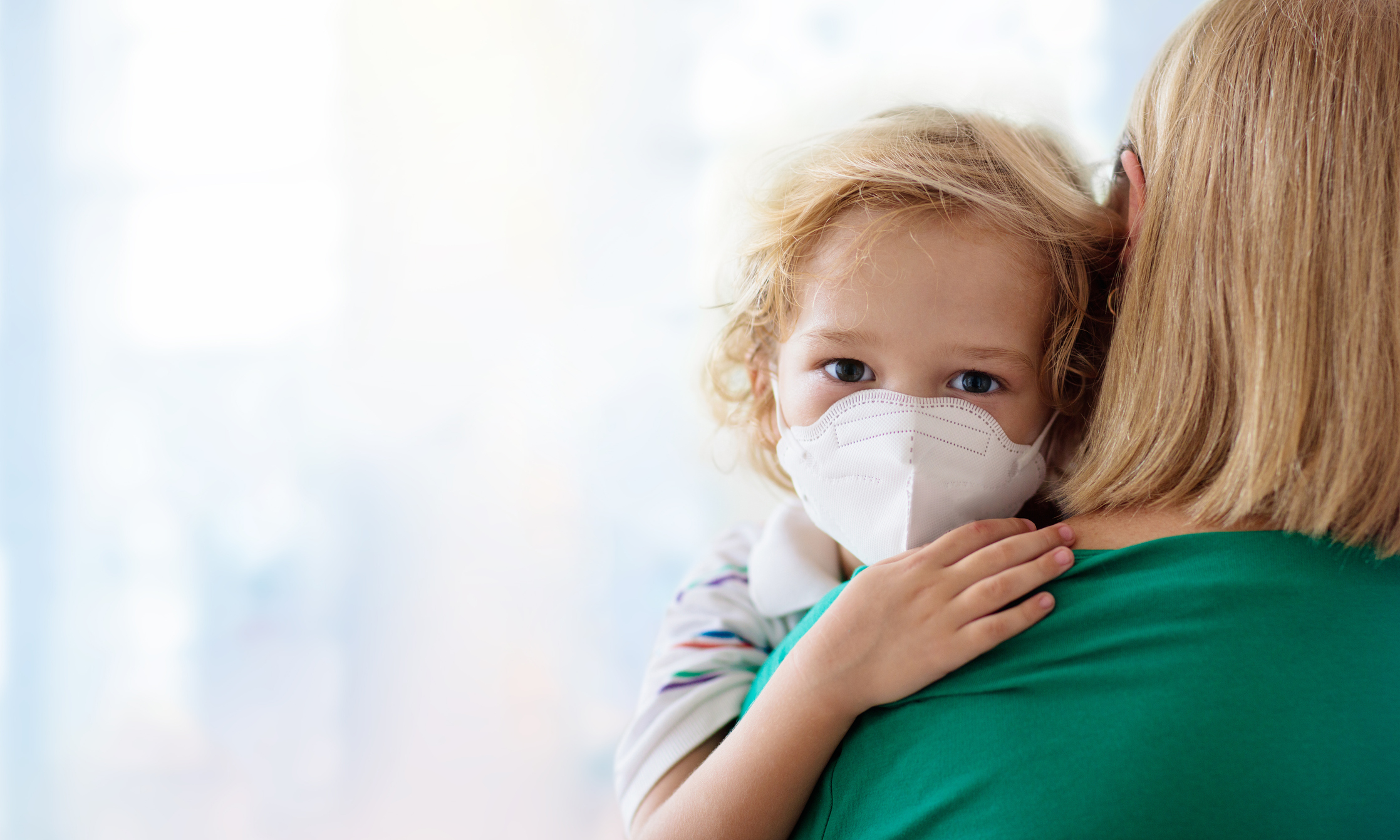 Mom holding masked toddler